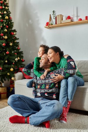 vertical shot of jolly african american family hugging warmly sitting next to Christmas tree