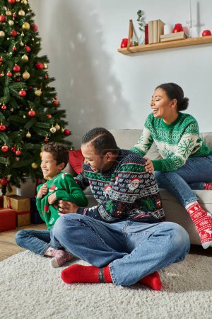 vertikale Aufnahme einer glücklichen afrikanisch-amerikanischen Familie, die neben dem Weihnachtsbaum lächelt und Spaß hat