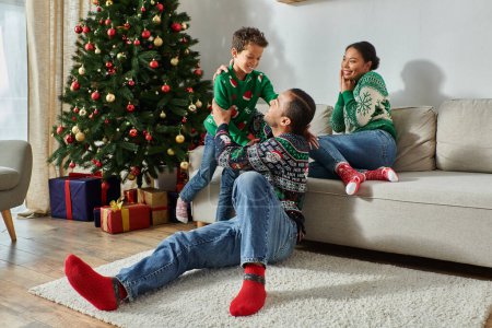 pretty african american woman looking happily at her husband and son next to Christmas tree