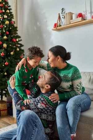 vertikale Aufnahme einer fröhlichen afrikanisch-amerikanischen Familie in lässigen Pullovern, die einander anlächeln, Weihnachten