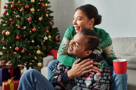happy african american couple hugging warmly with coffee cup in hand, looking away, Christmas