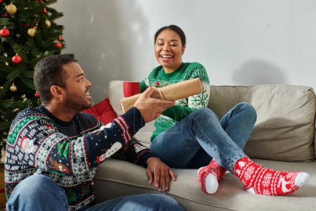 alegre afroamericano hombre dando regalo de Navidad a su hermosa esposa feliz, tiempo de calidad