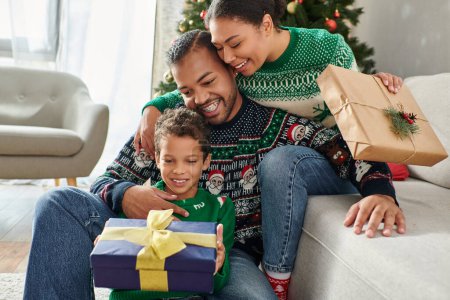 schöne freudige afrikanisch-amerikanische Familie tauscht Geschenke aus und umarmt sich herzlich, Weihnachten