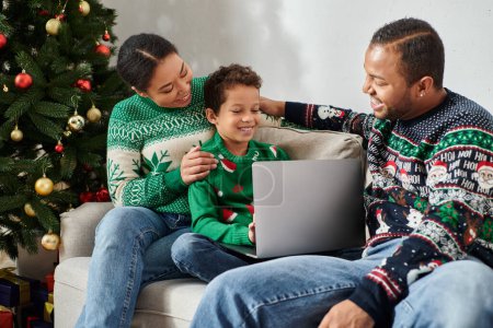 alegre afroamericano familia tener gran tiempo mientras ver la película en el ordenador portátil en la mañana de Navidad