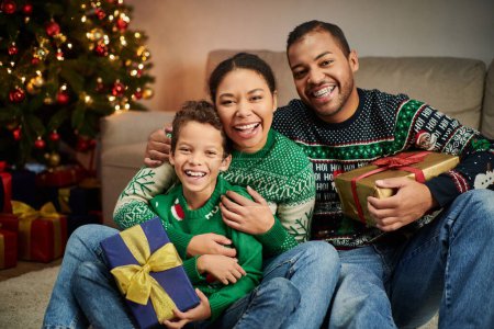 glückliche afrikanisch-amerikanische Familie umarmt sich herzlich neben dem Weihnachtsbaum und lächelt fröhlich in die Kamera