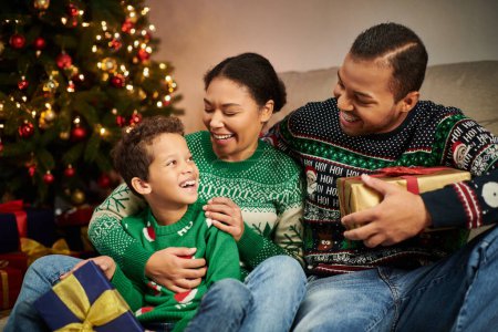 Foto de Familia afroamericana feliz sentada al lado del árbol de Navidad con guirnaldas y sonriéndose - Imagen libre de derechos