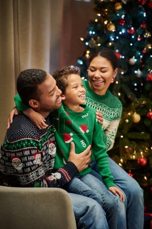 tiro vertical de la familia afroamericana alegre moderna abrazándose cálidamente y sonriendo felizmente, Navidad