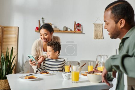 focus on african american mother and looking at mobile phone with blurred father in front of them