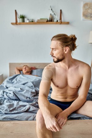 Téléchargez les photos : Bouleversé homme barbu en caleçon assis sur le lit près partenaire d'amour endormi, relation troublée - en image libre de droit