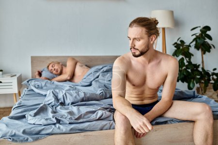 beleidigter bärtiger Schwuler in Unterhosen, der in der Nähe seines Liebespartners sitzt, der im Schlafzimmer liegt, gestörte Liebe