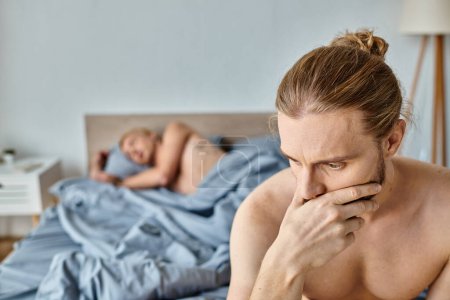 offended bearded gay man with hand near face near boyfriend sleeping in bedroom, frustration