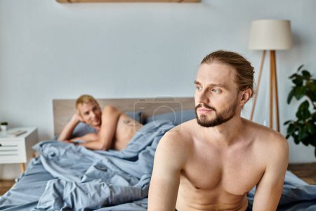 homme barbu rêveur et positif regardant loin près partenaire gay couché sur le lit, le bonheur et la sérénité