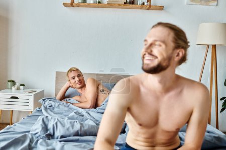 cheerful bearded gay man looking away near love partner lying in bedroom, harmonious relationship