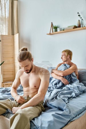 bearded gay man dressing up near offended love partner in bedroom in morning, trouble relationship