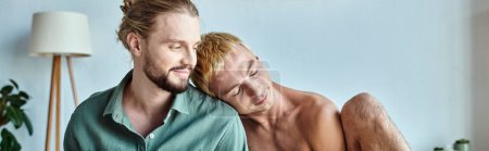 glücklicher schwuler Mann, der sich auf lächelnden bärtigen Freund stützt, der im modernen Schlafzimmer sitzt, Banner