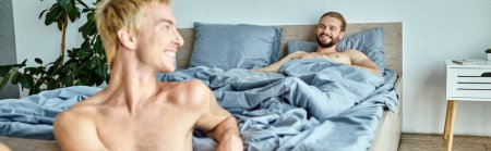 fröhlicher bärtiger schwuler Mann, der morgens auf dem Bett liegt und seinen lächelnden Freund ansieht, horizontales Banner