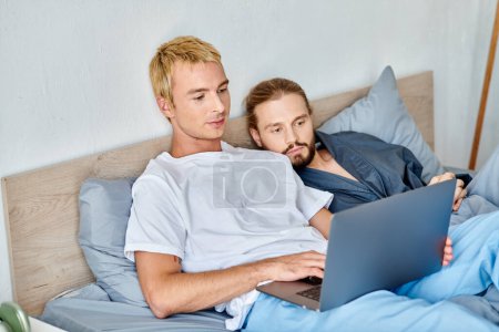 Téléchargez les photos : Concentré gay couple regarder romantique film sur portable dans chambre, matin loisirs sur lit - en image libre de droit