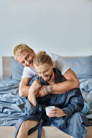 joyeux tatoué gay homme embrassant barbu copain avec tasse de café dans chambre, scène heureuse