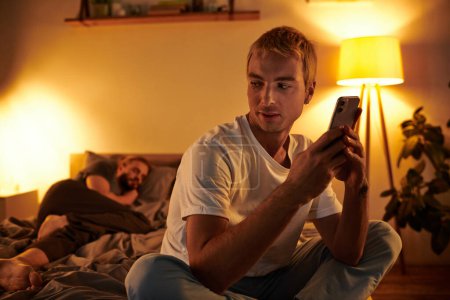 infidèle gay l'homme bavarder sur téléphone mobile près de l'amour partenaire dormir la nuit dans chambre