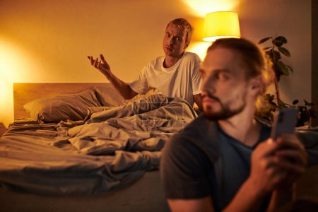Unzufriedener schwuler Mann streitet mit Freund Nachrichten auf Smartphone in der Nacht im Schlafzimmer, Ärger