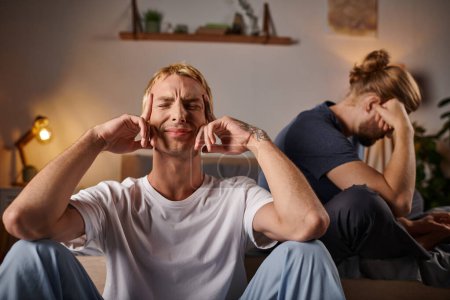 Photo for Depressed gay man sitting with closed eyes near boyfriend in bedroom at night, troubled relationship - Royalty Free Image