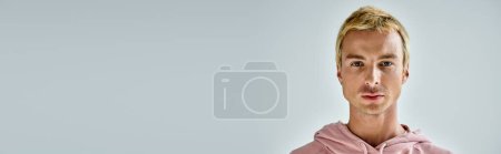 retrato de hombre carismático con el pelo rubio teñido mirando a la cámara en el fondo gris, pancarta
