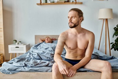Photo for Upset bearded man in underpants sitting and looking away near love partner sleeping in bedroom - Royalty Free Image