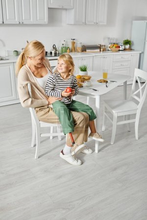 préscolaire fille avec prothèse jambe assis sur les tours de mère heureuse pendant le petit déjeuner dans la cuisine