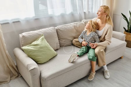 happy mother hugging daughter with prosthetic leg and sitting together on sofa in living room