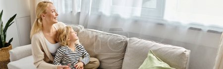 alegre madre abrazando hija en traje casual y sentados juntos en el sofá en la sala de estar, pancarta