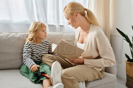 Blonde Mutter liest kleinem Mädchen mit Beinprothese Buch, während sie zusammen im Wohnzimmer sitzt