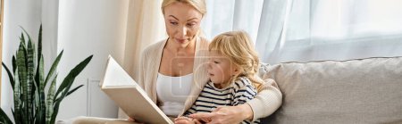 Téléchargez les photos : Blonde mère lecture livre à fille tout en étant assis ensemble dans le salon moderne, bannière - en image libre de droit