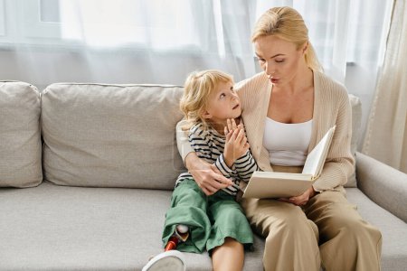 Blonde Mutter liest süßem Kind mit Beinprothese Buch, während sie zusammen im Wohnzimmer sitzt