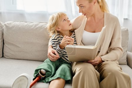 Blonde Mutter liest ihrem Kind mit Beinprothese Buch, während sie zusammen im Wohnzimmer sitzt
