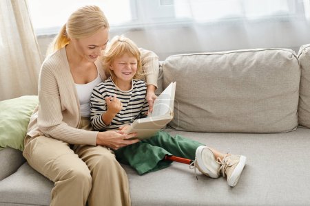 Mutter liest ihrer glücklichen Tochter mit Beinprothese Buch und sitzt zusammen im Wohnzimmer