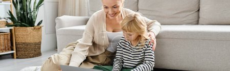 mujer rubia feliz viendo la película en el ordenador portátil cerca de la hija preescolar en la sala de estar moderna, pancarta