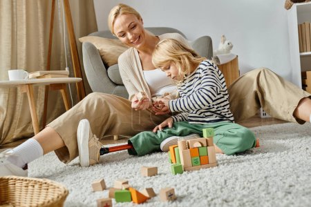 little girl with prosthetic leg sitting on carpet and playing with wooden toys near cheerful mother