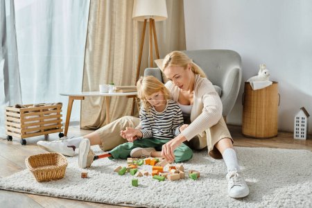 Blondes Mädchen mit Beinprothese sitzt auf Teppich und spielt mit Holzklötzen in der Nähe der Mutter zu Hause