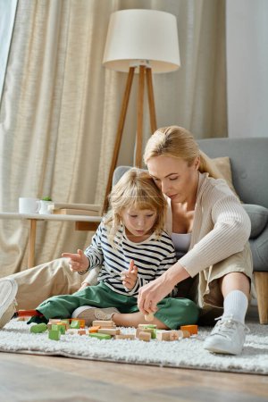 blonde girl with prosthetic leg sitting on carpet and playing with wooden blocks near caring mom
