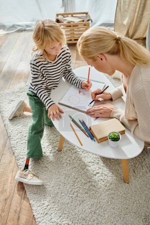 mother and child with prosthetic leg drawing together on paper with colorful pencils, quality time