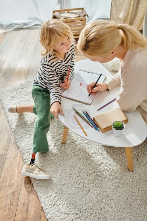Foto de Madre y niño con la pierna protésica dibujando juntos en papel con lápices de colores, tiempo de calidad - Imagen libre de derechos