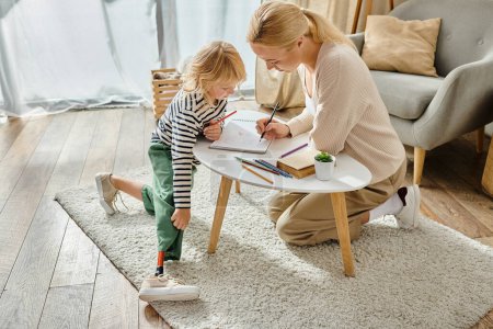 mother and daughter with prosthetic leg drawing on paper with colorful pencils, quality time