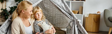 Téléchargez les photos : Mignonne fille tenant lapin jouet doux près de mère heureuse tout en étant assis ensemble dans la tente de jeu, bannière - en image libre de droit
