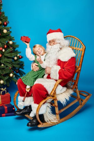 Foto de Chica feliz con la pierna prótesis sentado en vueltas de Santa Claus con caja de regalo al lado del árbol de Navidad - Imagen libre de derechos