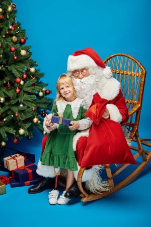 Foto de Alegre chica con prótesis pierna celebración presente cerca de Santa Claus junto a árbol de Navidad en azul - Imagen libre de derechos