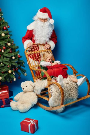 Santa Claus rocking chair with cute girl with prosthetic leg holding sack bag near Christmas tree