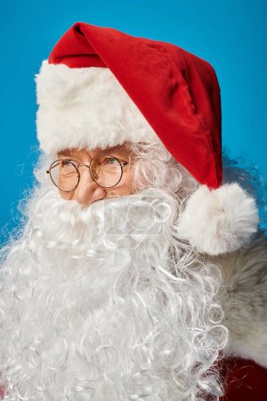 portrait du Père Noël heureux avec barbe blanche et lunettes regardant loin sur fond bleu