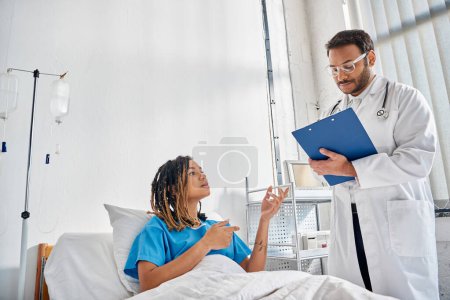 Téléchargez les photos : Jeune médecin indien regardant un patient afro-américain couché dans un service hospitalier, soins de santé - en image libre de droit