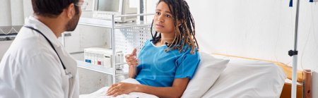 Foto de Atractiva mujer afroamericana enferma acostada en la cama de hospital hablando con el joven médico indio, pancarta - Imagen libre de derechos