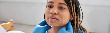 Téléchargez les photos : Jeune femme afro-américaine regardant son médecin indien alors qu'il examine ses ganglions lymphatiques, bannière - en image libre de droit